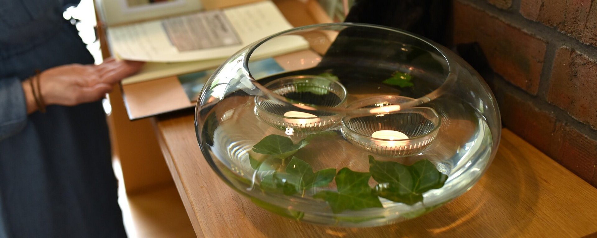 Auf einem Altar für eine Verstorbene im Hospiz steht eine mit Wasser gefüllte Vase, in der zwei Teelichter und Blätter schwimmen.
