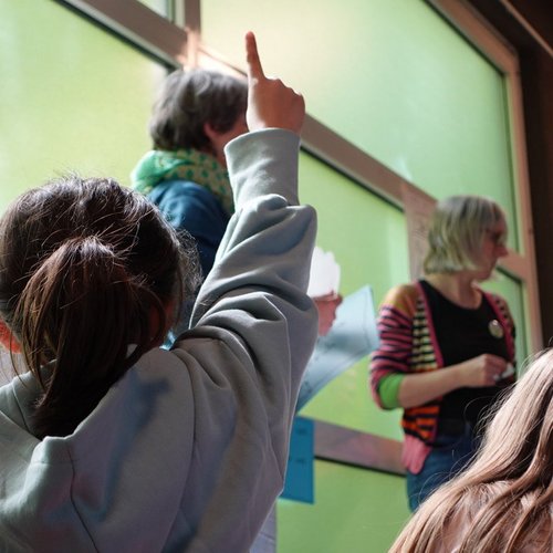 Kind von hinten, zeigt den Finger auf, weil es etwas sagen möchte