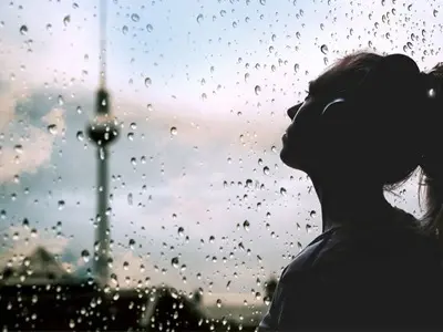 Profil einer jungen Frau, die durch das regennasse Fenster in den Himmel schaut. Im Hintergrund der Fernsehturm am Alexanderplatz.