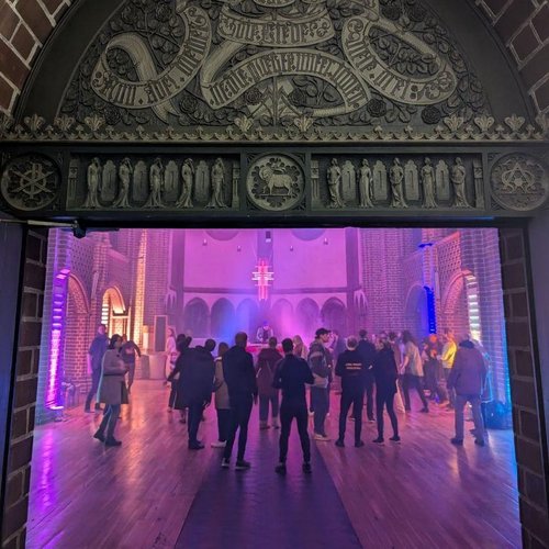 Blick in die geöffnete Kirchentür mit Partylicht und Tanzenden in der Kirche