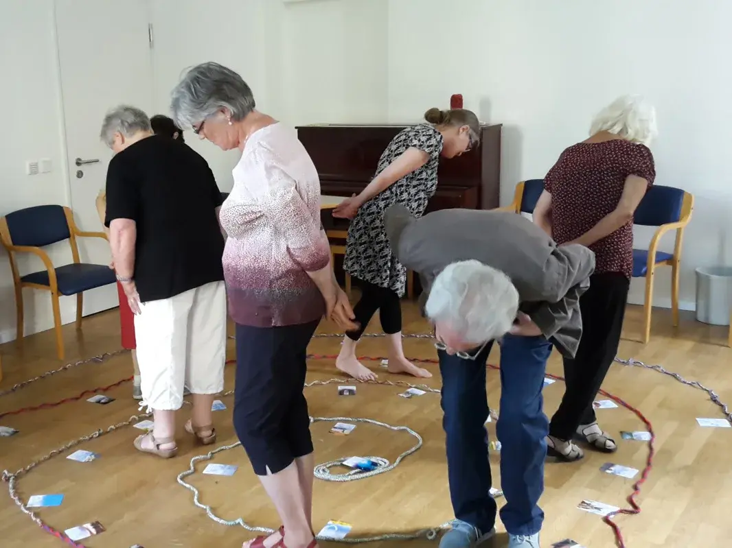 Gruppe von 5 Personen macht eine Übung im Raum - alle schauen suchend auf den Boden