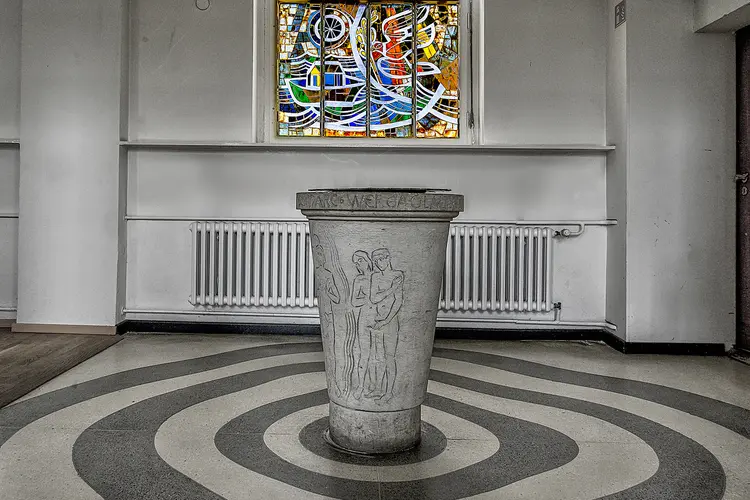 Taufbecken in der Südender Kirche und das bunt gestaltete Fenster darüber mit der Arche Noah und der großen Taube mit dem Ölzweig