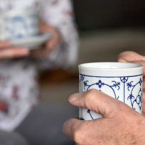 Sicht auf die Hände zweier älterer Personen, die jeweils einen Kaffeebecher halten