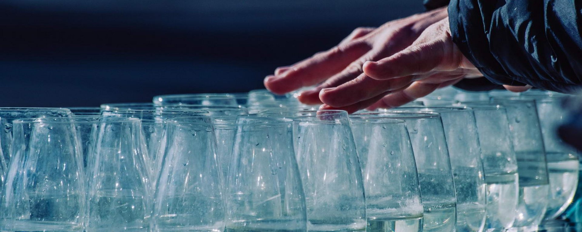 Weingläser mit Wasser gefüllt - Hände streichen über den Rand der Gläser, um Töne zu erzeugen