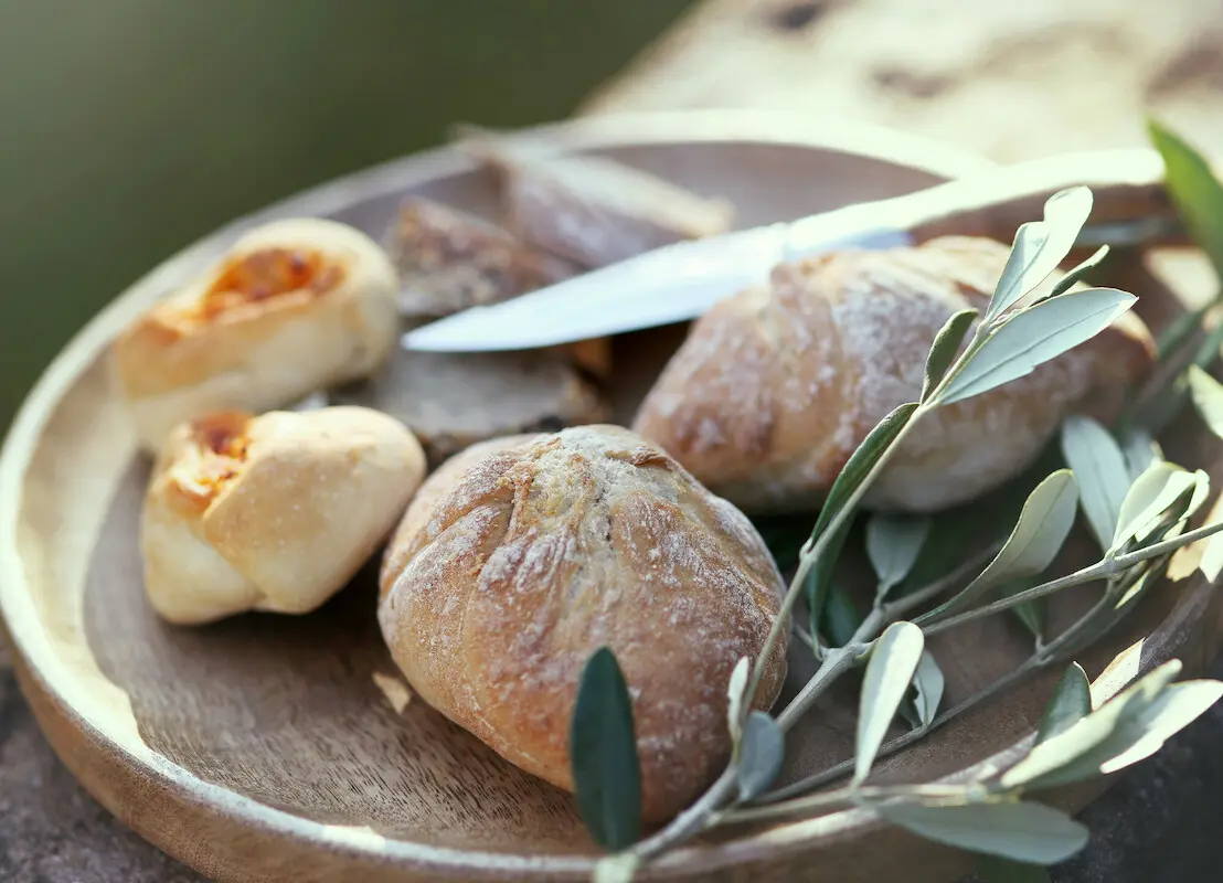 Teller mit frisch gebackenen Brötchen, einem Messer und einem Olivenzweig