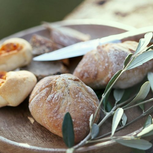 Teller mit frisch gebackenen Brötchen, einem Messer und einem Olivenzweig