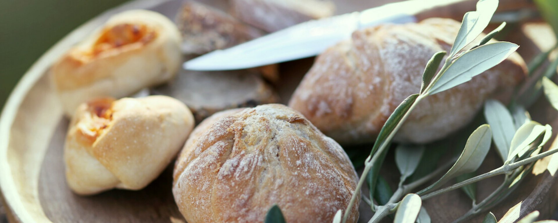 Teller mit frisch gebackenen Brötchen, einem Messer und einem Olivenzweig